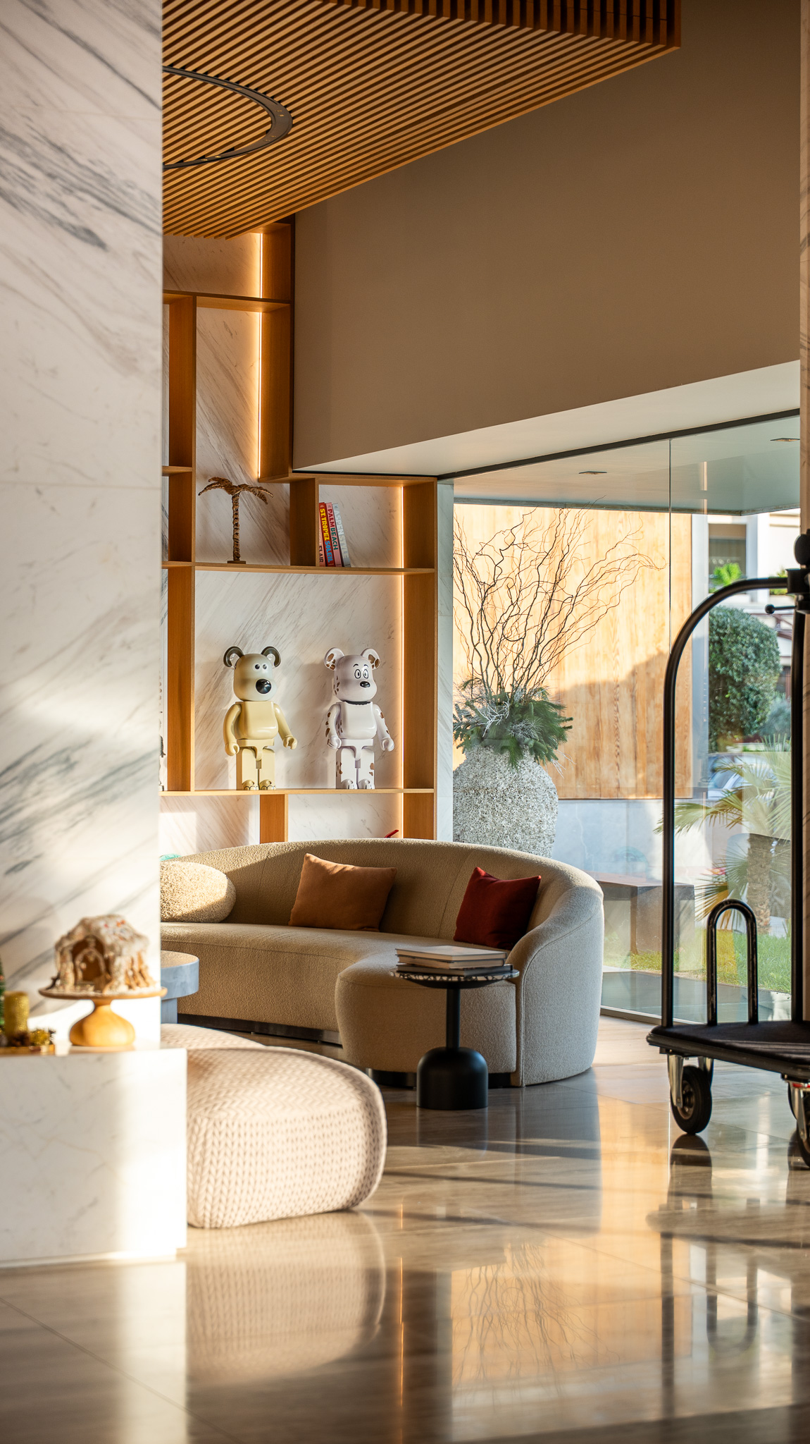 Dusit Suites Athens, sunlit lobby lounge with curved boucle sofa and marble column
